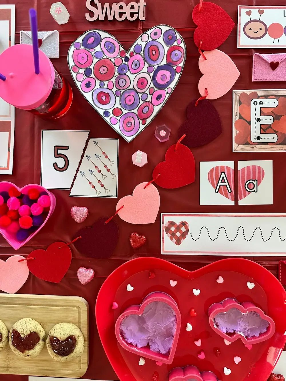 Valentine's Day-themed items including a heart-shaped cookie, pink drink with a straw, and decorative hearts on a red background.